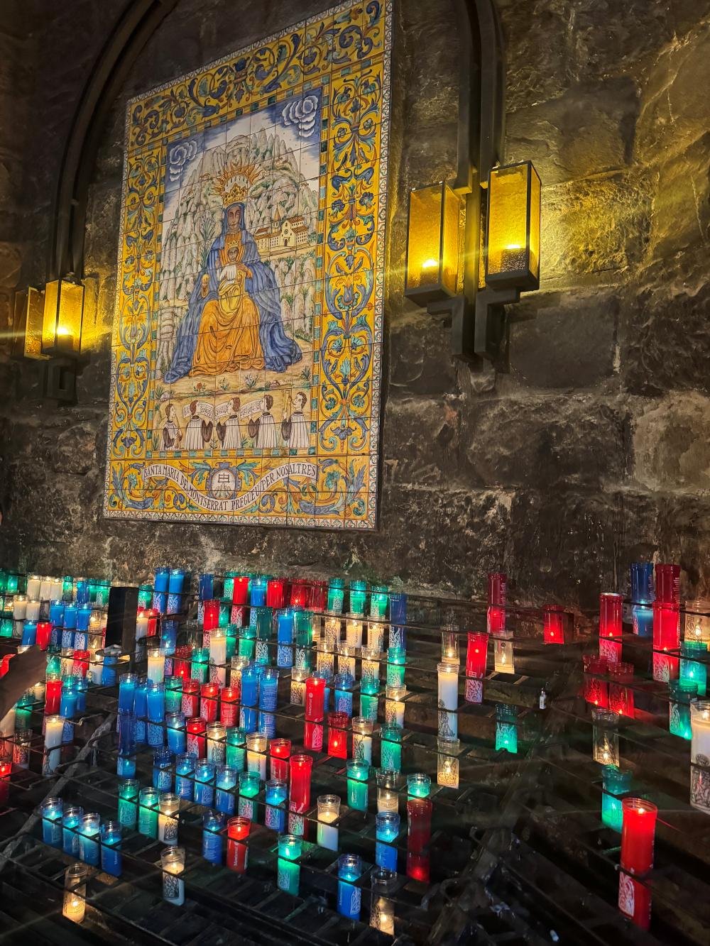 Velas votivas junto a un azulejo de la Virgen de Montserrat